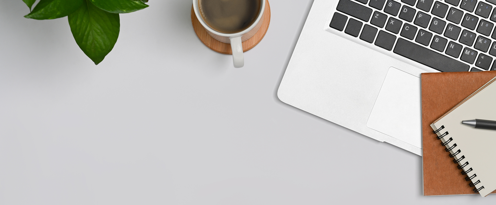 top view of white table with laptop, notebooks, a pen, coffee, and a plant